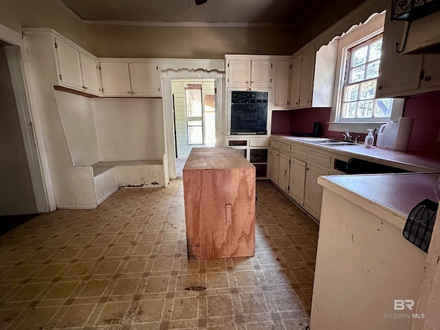 kitchen with black oven, sink, a center island, crown molding, and ceiling fan