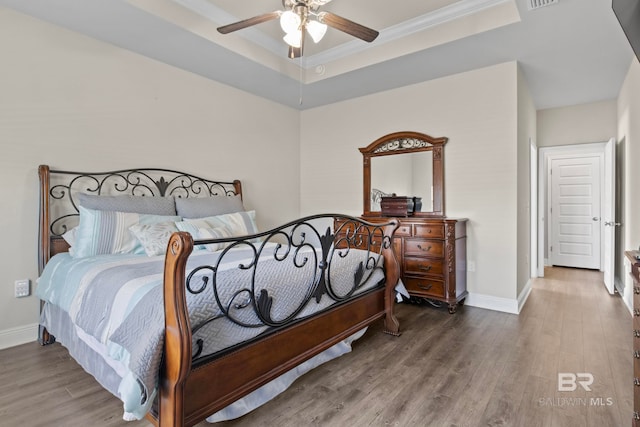 bedroom with hardwood / wood-style floors, a tray ceiling, ceiling fan, and ornamental molding