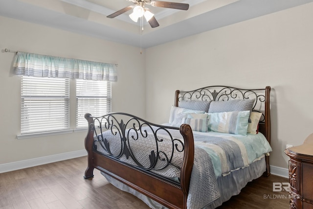 bedroom with hardwood / wood-style floors, ceiling fan, and a tray ceiling