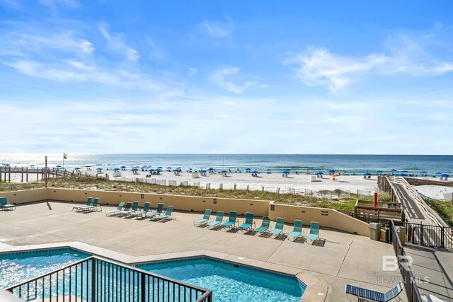 view of pool featuring a water view, a beach view, and a patio