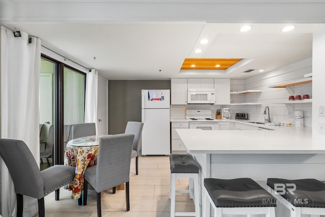 kitchen featuring kitchen peninsula, white appliances, sink, white cabinets, and a breakfast bar area