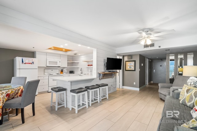 kitchen featuring white cabinetry, sink, kitchen peninsula, white appliances, and a breakfast bar area