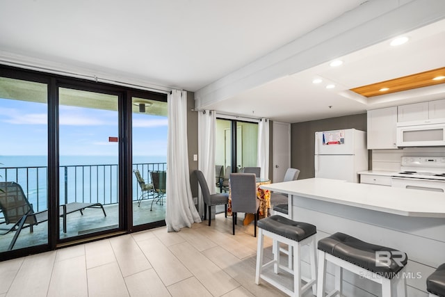 kitchen with floor to ceiling windows, white cabinetry, a kitchen breakfast bar, white appliances, and a water view