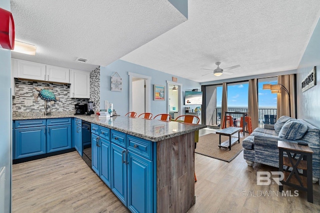 kitchen featuring black dishwasher, decorative backsplash, blue cabinets, light wood-type flooring, and a peninsula