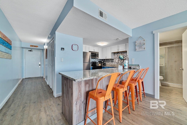 kitchen featuring a peninsula, light wood-style floors, visible vents, and stainless steel appliances