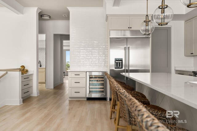 kitchen with light hardwood / wood-style flooring, light stone counters, beverage cooler, stainless steel built in refrigerator, and hanging light fixtures