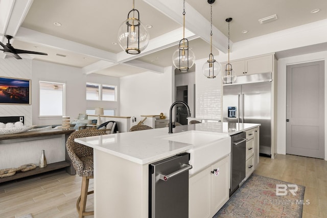 kitchen with light wood-type flooring, light stone countertops, white cabinetry, stainless steel appliances, and a center island with sink