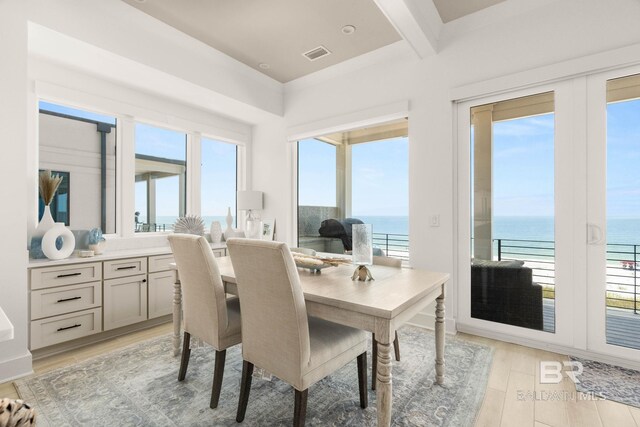 dining room with light hardwood / wood-style flooring, a healthy amount of sunlight, and a water view