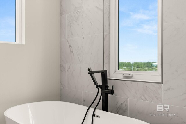 bathroom featuring a washtub and tile walls