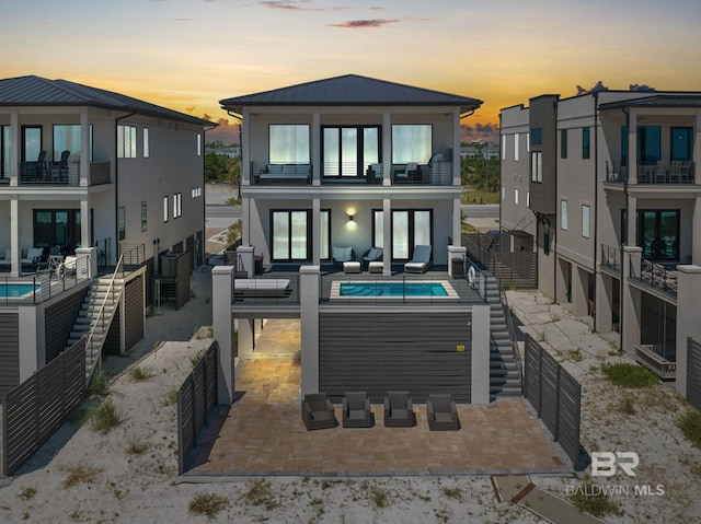 back house at dusk with a balcony, a patio area, and a pool with hot tub