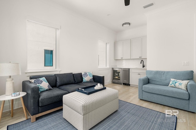 living room with sink, light hardwood / wood-style floors, wine cooler, and ornamental molding