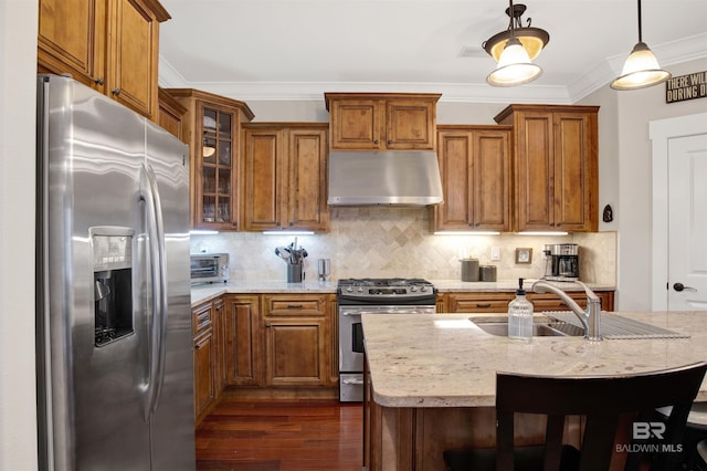 17541 Council Oaks Ln, Bon Secour, AL 36511 - kitchen with appliances with stainless steel finishes, under cabinet range hood, brown cabinetry, dark wood finished floors, and ornamental molding