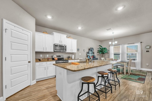 kitchen featuring stainless steel appliances, a sink, light wood finished floors, stone counters, and baseboards