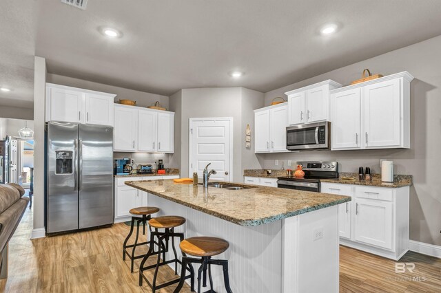 kitchen with appliances with stainless steel finishes, a sink, light wood-type flooring, baseboards, and white cabinetry