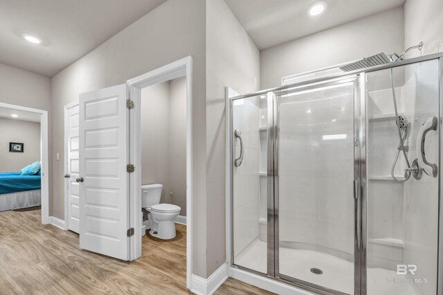 ensuite bathroom with wood finished floors, a stall shower, toilet, baseboards, and recessed lighting