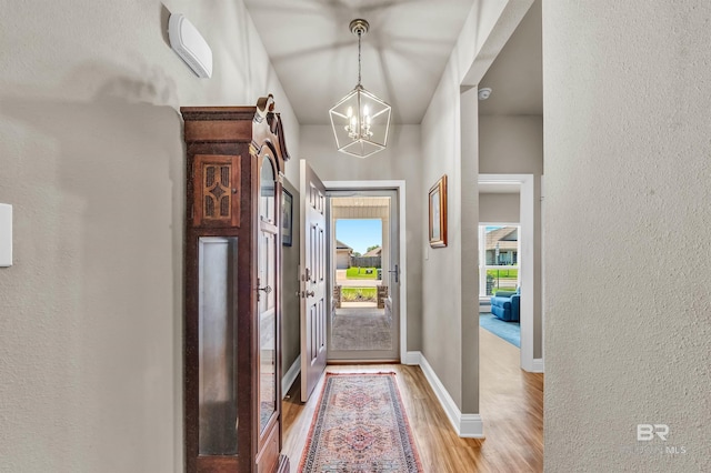 foyer entrance with a chandelier, light wood-style floors, a textured wall, and baseboards