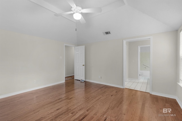 empty room featuring wood finished floors, baseboards, visible vents, ceiling fan, and vaulted ceiling