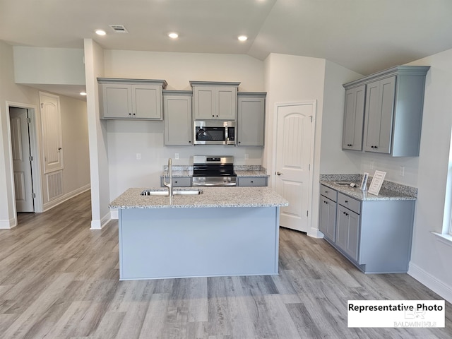 kitchen featuring a center island with sink, sink, gray cabinetry, stainless steel appliances, and light stone counters