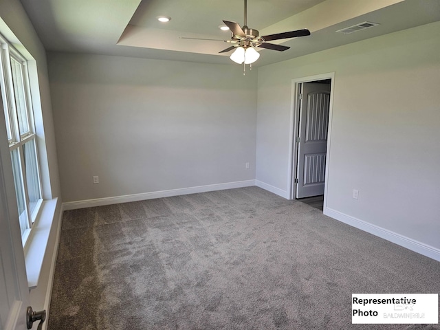 carpeted spare room with ceiling fan and a raised ceiling