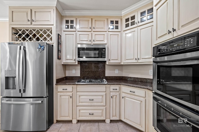9791 Aspen Cir, Spanish Fort, AL 36527 - kitchen with stainless steel appliances, cream cabinetry, light tile patterned floors, dark stone counters, and glass insert cabinets