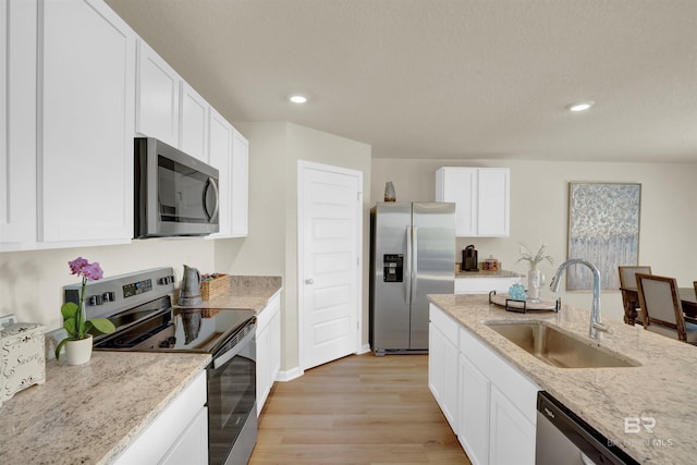 kitchen with sink, light hardwood / wood-style flooring, appliances with stainless steel finishes, white cabinetry, and light stone countertops