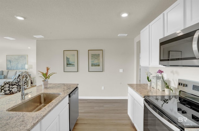 kitchen with sink, light stone counters, light hardwood / wood-style flooring, appliances with stainless steel finishes, and white cabinets