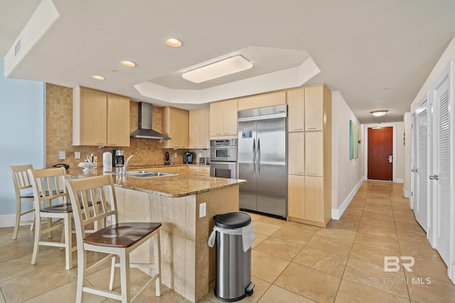 28107 Perdido Beach Blvd Unit D209, Orange Beach, AL 36561 - kitchen with appliances with stainless steel finishes, wall chimney range hood, a raised ceiling, light brown cabinetry, and recessed lighting