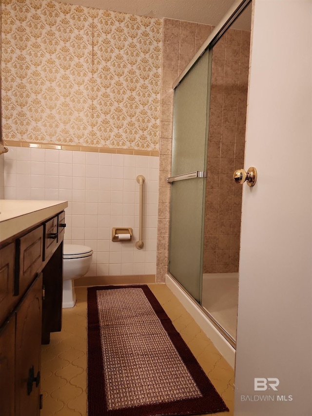 bathroom with a shower with door, vanity, tile walls, and toilet