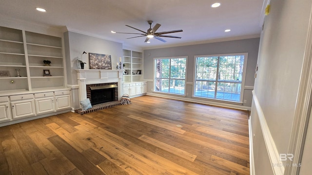 unfurnished living room with built in shelves, light hardwood / wood-style flooring, ornamental molding, and a brick fireplace