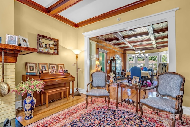 sitting room featuring wood-type flooring, beamed ceiling, coffered ceiling, an inviting chandelier, and ornamental molding