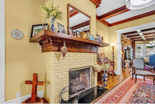 living room featuring coffered ceiling, a brick fireplace, beamed ceiling, wood-type flooring, and a chandelier