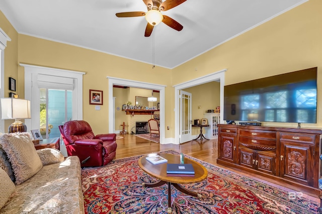 living room featuring ornamental molding, light wood-type flooring, ceiling fan, and a brick fireplace