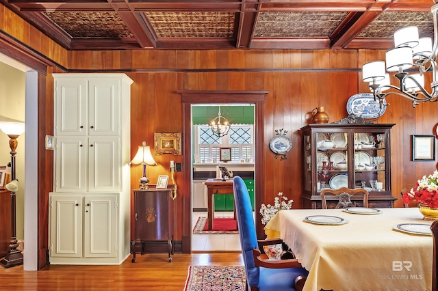 dining space featuring an inviting chandelier, light wood-type flooring, wood walls, and coffered ceiling