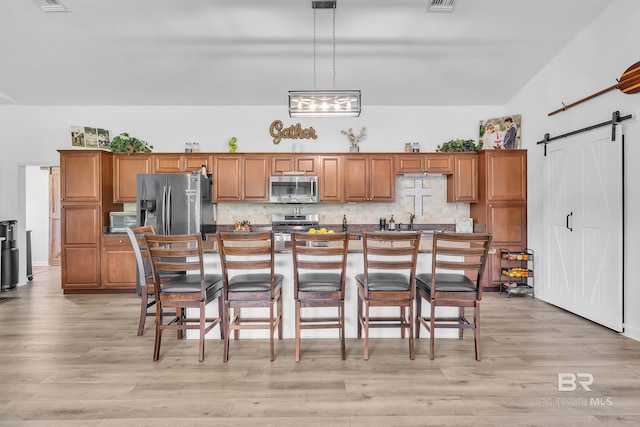 kitchen featuring brown cabinetry, a barn door, stainless steel appliances, and light wood-type flooring