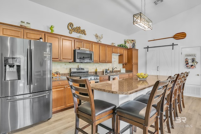 kitchen with light wood finished floors, appliances with stainless steel finishes, a barn door, and brown cabinets
