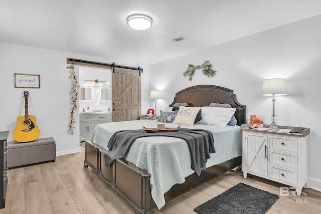 bedroom with baseboards, a barn door, light wood-type flooring, and visible vents