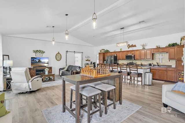 dining space featuring visible vents, a barn door, lofted ceiling with beams, and light wood-style flooring