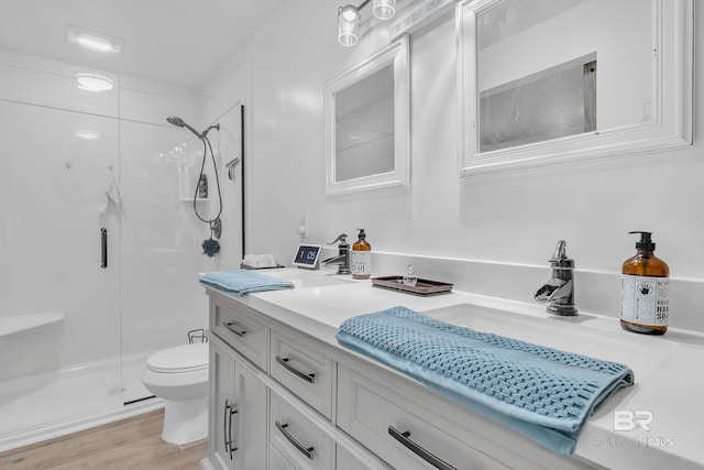 bathroom with double vanity, toilet, wood finished floors, a sink, and a shower stall