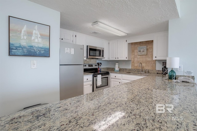 kitchen featuring a sink, light stone counters, appliances with stainless steel finishes, and white cabinetry