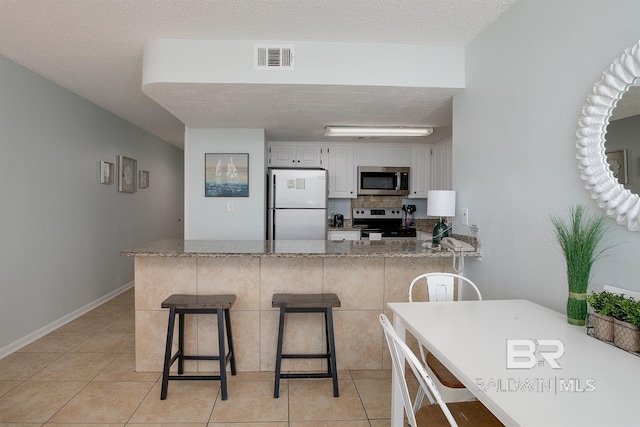 kitchen featuring visible vents, a breakfast bar, a peninsula, appliances with stainless steel finishes, and a textured ceiling