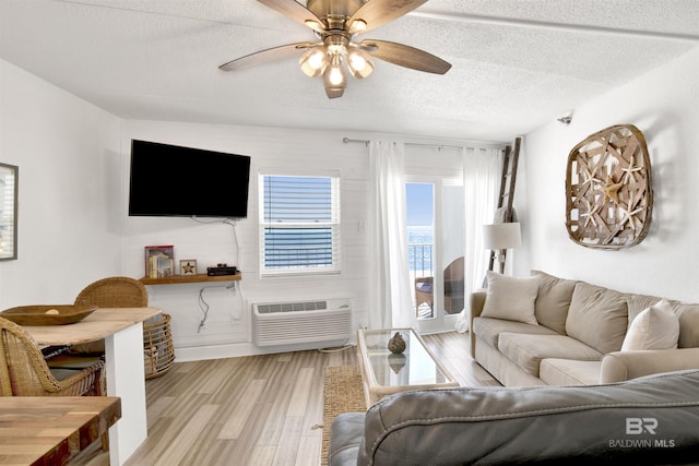 living room with a textured ceiling, an AC wall unit, a ceiling fan, and light wood-style floors