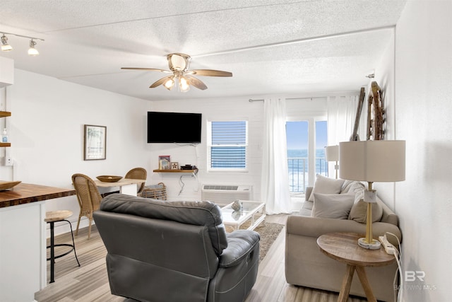 living area with light wood-style floors, an AC wall unit, ceiling fan, and a textured ceiling