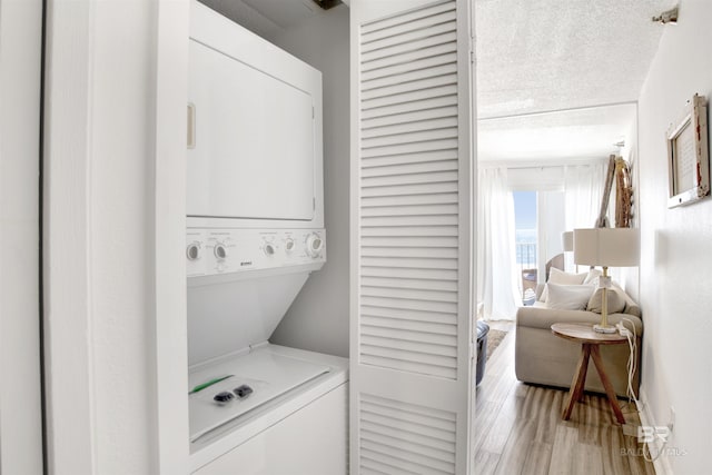 laundry room featuring stacked washer / dryer, laundry area, a textured ceiling, and light wood finished floors