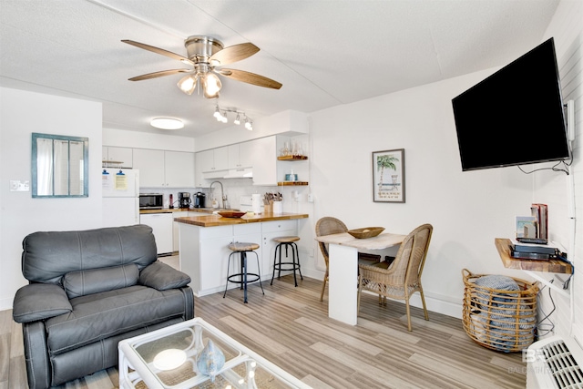 living room featuring light wood-style flooring, baseboards, and ceiling fan