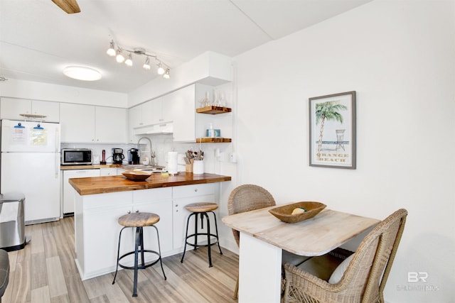 kitchen featuring a breakfast bar area, open shelves, wooden counters, white appliances, and a peninsula