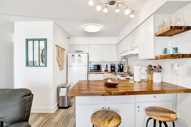 kitchen with under cabinet range hood, a peninsula, white appliances, wood counters, and open shelves