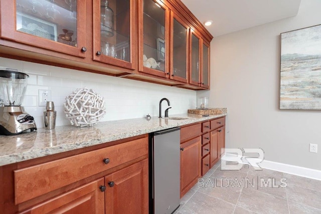 kitchen with brown cabinets, tasteful backsplash, glass insert cabinets, light stone countertops, and baseboards