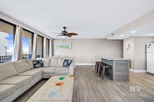 living area featuring light wood finished floors, a ceiling fan, visible vents, and baseboards