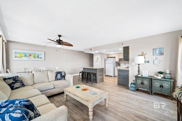 living room featuring ceiling fan, a textured ceiling, visible vents, baseboards, and light wood finished floors