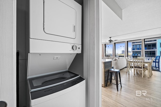 laundry area featuring a ceiling fan, stacked washer / dryer, laundry area, and light wood-style flooring